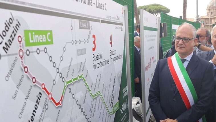 Il sindaco di Roma Roberto Gualtieri, con fascia tricolore, osserva un pannello dei lavori della Metro C che mostra il tracciato e le stazioni in costruzione vicino al cantiere di Piazza Venezia.