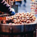 Un venditore prepara caldarroste su un grande braciere: il prezzo segnalato è 5,00 €. Scene tipiche del weekend di Tutti i Santi, tra mercatini e passeggiate nei quartieri della Capitale.