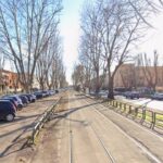 Vista centrale dei binari del tram su viale Palmiro Togliatti a Roma, con alberi spogli ai lati, auto parcheggiate e luce diurna.