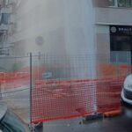 “Geyser d’acqua da tubatura rotta in viale degli Ammiragli a Roma, spruzzo fino ai piani alti davanti a negozi e veicoli, area transennata.”