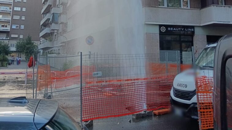 “Geyser d’acqua da tubatura rotta in viale degli Ammiragli a Roma, spruzzo fino ai piani alti davanti a negozi e veicoli, area transennata.”