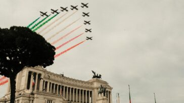 Formazione di aerei delle Frecce Tricolori che vola sopra l’Altare della Patria a Roma lasciando scie di fumo verde, bianco e rosso nel cielo.