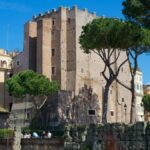 Veduta diurna della Torre dei Conti a Roma, circondata da pini e palazzi, con cielo azzurro limpido sullo sfondo