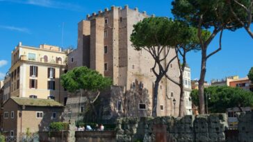 Veduta diurna della Torre dei Conti a Roma, circondata da pini e palazzi, con cielo azzurro limpido sullo sfondo