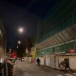 Via Campania di notte, con il liceo Righi a sinistra e un edificio coperto da impalcature a destra; alcuni ragazzi incappucciati corrono vicino alle transenne del cantiere.