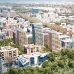 Veduta aerea del quartiere Tor Marancia a Roma con il render di cinque nuove torri residenziali moderne, alte e vetrate, circondate da edifici più bassi e da un’ampia area verde in primo piano.