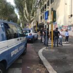 Mezzi della polizia e agenti schierati in strada durante un intervento, con pattuglie, unità cinofile e residenti presenti nell’area.