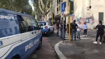 Mezzi della polizia e agenti schierati in strada durante un intervento, con pattuglie, unità cinofile e residenti presenti nell’area.
