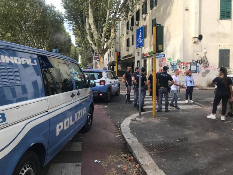 Mezzi della polizia e agenti schierati in strada durante un intervento, con pattuglie, unità cinofile e residenti presenti nell’area.