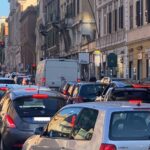 Traffico congestionato su via Appia Nuova a Roma con auto in fila e semafori rossi.