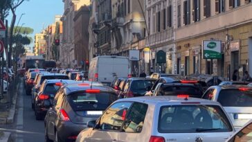 Traffico congestionato su via Appia Nuova a Roma con auto in fila e semafori rossi.