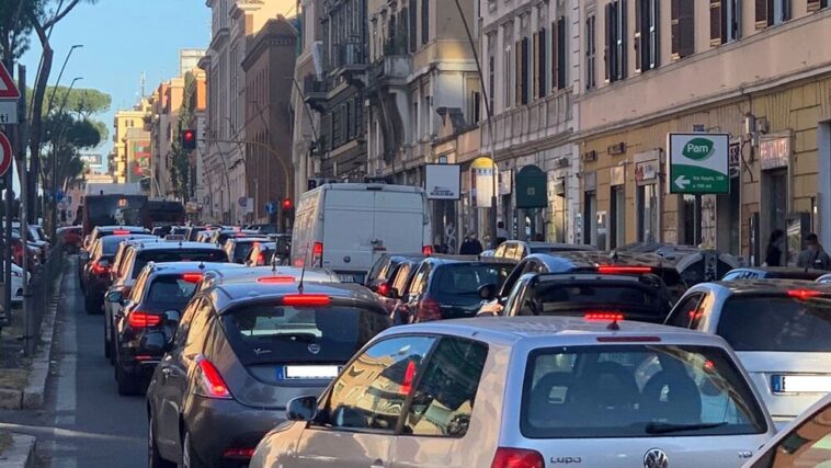 Traffico congestionato su via Appia Nuova a Roma con auto in fila e semafori rossi.