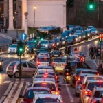 Traffico intenso a Roma con lunghe code di auto e motorini vicino al centro, in una strada affollata al tramonto.