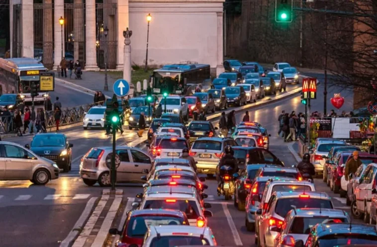 Traffico intenso a Roma con lunghe code di auto e motorini vicino al centro, in una strada affollata al tramonto.