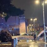 Albero caduto ai Fori Imperiali vicino al Colosseo, con vigili del fuoco e passanti che osservano l’area transennata durante una notte di pioggia.