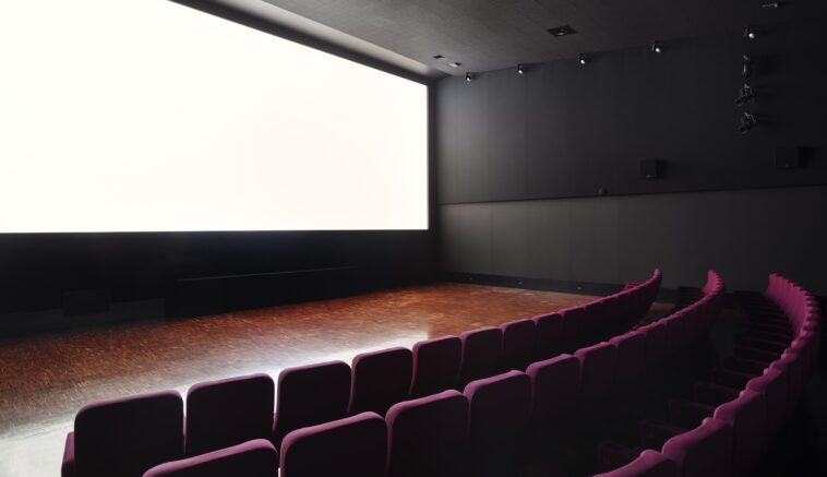 Interno della sala del Cinema Troisi con schermo luminoso e poltrone viola disposte a semicerchio.