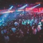 Folla in una discoteca romana illuminata da luci colorate durante una serata affollata.