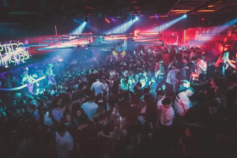 Folla in una discoteca romana illuminata da luci colorate durante una serata affollata.