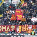 Tifosi della Roma sugli spalti con bandiere e striscioni giallorossi durante una trasferta.
