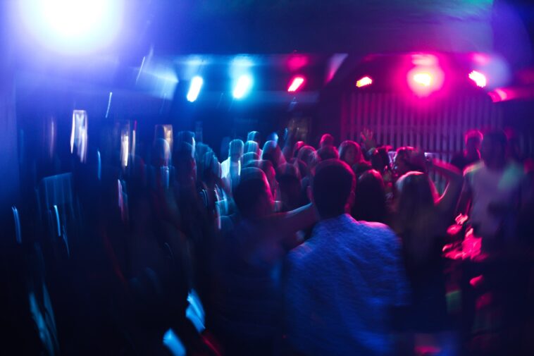 Folla di giovani che balla in una discoteca con luci blu e rosa sfocate.