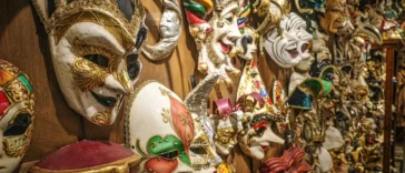 Maschera di Carnevale rosa e oro appoggiata su un tavolo con stelle filanti colorate.