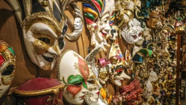 Maschera di Carnevale rosa e oro appoggiata su un tavolo con stelle filanti colorate.