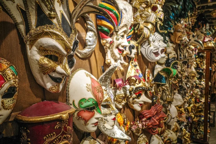 Maschera di Carnevale rosa e oro appoggiata su un tavolo con stelle filanti colorate.