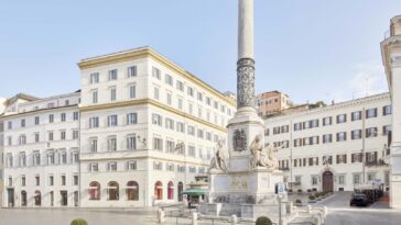 Vista di piazza Mignanelli a Roma con la Colonna dell’Immacolata e gli edifici storici circostanti in una giornata luminosa.
