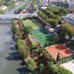 Veduta aerea dei campi sportivi e delle aree verdi lungo il Tevere, con ponte e palazzi del quartiere Flaminio sullo sfondo.