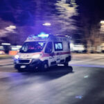 Ambulanza in corsa di notte con sirene accese su una strada urbana semideserta.
