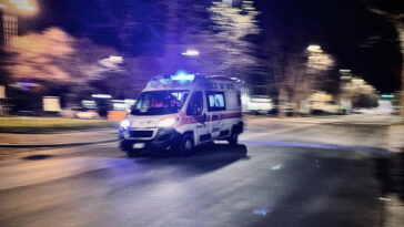 Ambulanza in corsa di notte con sirene accese su una strada urbana semideserta.