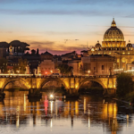 Tramonto su Roma con vista su Ponte Sant’Angelo, il Tevere e la Basilica di San Pietro illuminata.