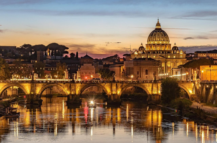 Tramonto su Roma con vista su Ponte Sant’Angelo, il Tevere e la Basilica di San Pietro illuminata.