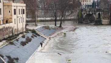 Banchine del Tevere allagate a Roma, con una persona sotto la pioggia e l’acqua del fiume a ridosso degli argini.