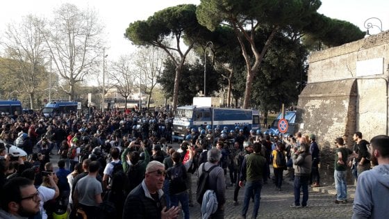 Folla radunata in strada a Roma durante un corteo, con diversi mezzi della polizia e agenti in tenuta antisommossa schierati per gestire la manifestazione.