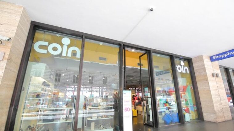 Ingresso del negozio Coin di via Giolitti a Roma, con vetrate e cartelli promozionali visibili dall’esterno.