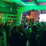 Locale romano affollato con maxi schermo acceso durante una serata dedicata al Festival di Sanremo.