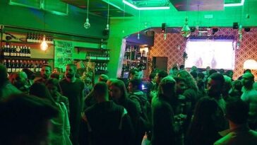 Locale romano affollato con maxi schermo acceso durante una serata dedicata al Festival di Sanremo.