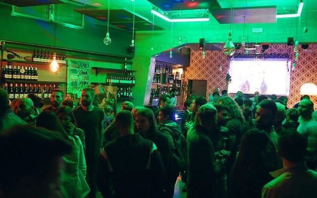 Locale romano affollato con maxi schermo acceso durante una serata dedicata al Festival di Sanremo.