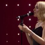 Cantante sul palco di Sanremo mentre si esibisce al microfono, con luci soffuse sullo sfondo.