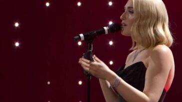 Cantante sul palco di Sanremo mentre si esibisce al microfono, con luci soffuse sullo sfondo.