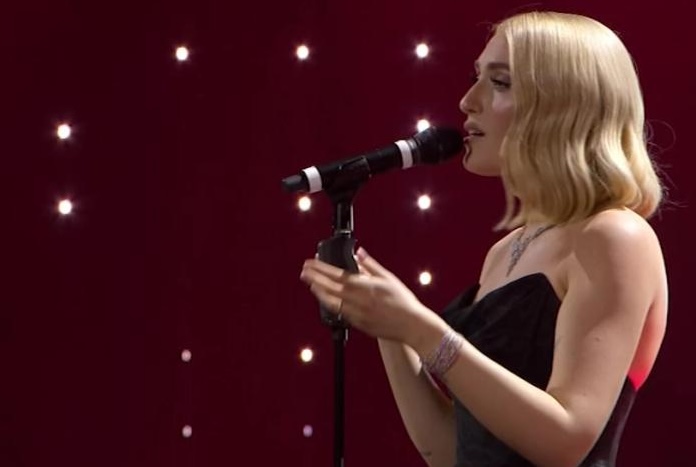 Cantante sul palco di Sanremo mentre si esibisce al microfono, con luci soffuse sullo sfondo.