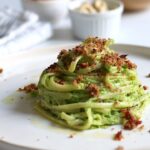 Piatto di spaghetti vegani con crema verde e crumble croccante serviti su un piatto chiaro.