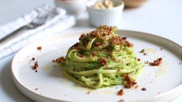 Piatto di spaghetti vegani con crema verde e crumble croccante serviti su un piatto chiaro.