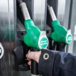 Primo piano di una mano che impugna una pistola per il rifornimento di benzina presso una pompa di servizio.