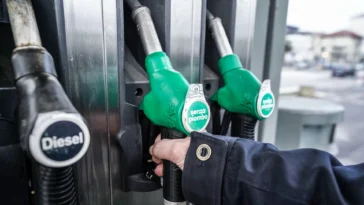 Primo piano di una mano che impugna una pistola per il rifornimento di benzina presso una pompa di servizio.