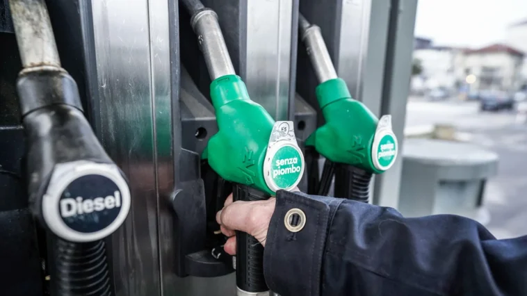 Primo piano di una mano che impugna una pistola per il rifornimento di benzina presso una pompa di servizio.