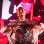 Il rapper Luchè durante un concerto dal vivo sul palco con luci rosse sullo sfondo.