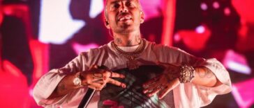 Il rapper Luchè durante un concerto dal vivo sul palco con luci rosse sullo sfondo.