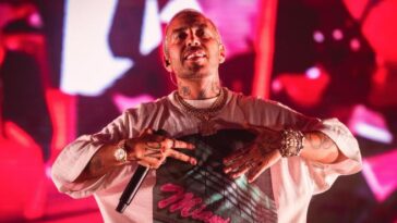 Il rapper Luchè durante un concerto dal vivo sul palco con luci rosse sullo sfondo.